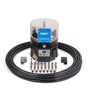 Obraz jest ucieleśnieniem kompaktowej, zintegrowanej automatyzacji smarowania, kt&oacute;re są synonimami zaawansowanych system&oacute;w SKF. Kompozycja łączy w sobie sterylny, high-tech'owy wizerunek kompletnej jednostki pompującej TLMP z profesjonalizmem i dostępnością, jakie budzi autoryzowany polski dystrybutor DAKAM. Dominują w niej ikoniczne barwy SKF &ndash; intensywny niebieski &ndash; oraz przezroczyste elementy zbiornika. W centrum uwagi, na czystej, industrialnej powierzchni (np. metalowym stole warsztatowym lub białym tle), znajduje się automatyczna smarownica wielopunktowa SKF TLMP 1018/24DC: &bull;	Zintegrowana jednostka: Prezentowana jest kompletna, kompaktowa jednostka, kt&oacute;ra łączy w sobie pompę, zbiornik i sterownik. &bull;	Kluczowy detal &ndash; 18 wyjść: Najważniejszy element wizualny &ndash; wyraźnie widoczny blok dystrybucyjny z maksymalnie 18 wyjściami (portami). To wizualnie komunikuje jej przeznaczenie do bezpośredniego smarowania wielopunktowego wielu element&oacute;w maszyny z jednej, centralnej jednostki. &bull;	Przezroczysty zbiornik: Widoczny jest przezroczysty zbiornik na smar (o pojemności ok. 1 litra) z mieszadłem, co umożliwia łatwą wizualną kontrolę poziomu środka smarnego. &bull;	Zasilanie 24V DC: Widoczne jest przyłącze elektryczne, co podkreśla zasilanie 24V DC i możliwość integracji ze sterownikiem PLC maszyny (sterowanie cyklami pracy bezpośrednio z automatyki maszyny). &bull;	Marka Premium: Na solidnej obudowie (niebieskiej lub czarnej) widoczne jest wyraźne, oryginalne logo "SKF" oraz oznaczenie modelu "TLMP 1018", co jest gwarancją autentyczności i światowej klasy technologii. Tło jest subtelnie rozmyte (efekt bokeh), ale jednoznacznie wskazuje na profesjonalną dystrybucję na terenie Polski: &bull;	Nowoczesny magazyn DAKAM: W tle widać rzędy wysokich regał&oacute;w magazynowych, wypełnionych uporządkowanymi, oryginalnymi, niebieskimi opakowaniami SKF. Duża ilość towaru na stanie wizualnie potwierdza status "sprawdzonego dystrybutora". &bull;	Logo Dystrybutora: W dyskretnym, ale widocznym miejscu umieszczone jest logo DAKAM, z dopiskiem "Autoryzowane Centrum System&oacute;w Smarowania" lub "Autoryzowany Dystrybutor SKF". Obraz niesie jasny komunikat: "Jako autoryzowany polski dystrybutor DAKAM, posiadamy na stanie kompaktowe smarownice wielopunktowe SKF TLMP 1018/24DC, idealne do automatycznego smarowania wielu punkt&oacute;w w maszynach, sterowane bezpośrednio z PLC".