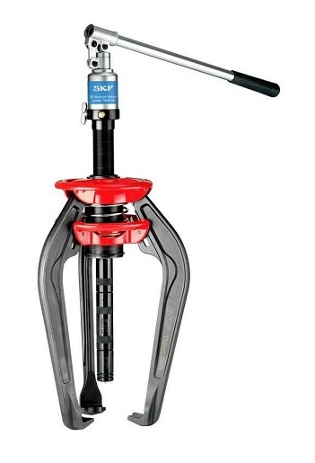 Hydrauliczny Ściągacz SKF EasyPull TMMA 75H w DAKAM Obraz jest ucieleśnieniem mobilności, ergonomii i zintegrowanej mocy. Prezentuje flagowy model z serii EasyPull &ndash; SKF TMMA 75H &ndash; jako kompletne, samowystarczalne urządzenie, kt&oacute;re eliminuje potrzebę stosowania zewnętrznych pomp i węży. Kompozycja łączy nowoczesny design narzędzia z profesjonalizmem autoryzowanego polskiego dystrybutora DAKAM. Dominują w niej barwy: czarna matowa stal (korpus/siłownik), srebrne ramiona oraz charakterystyczne akcenty (czerwone/niebieskie) marki SKF. W centrum uwagi, na czystym stole warsztatowym, stoi gotowy do pracy ściągacz SKF TMMA 75H: &bull;	Zintegrowany Siłownik i Pompa: To najważniejszy wyr&oacute;żnik wizualny. Widoczny jest solidny, czarny korpus, kt&oacute;ry mieści w sobie zar&oacute;wno siłownik hydrauliczny, jak i pompę. Brak plątaniny węży zewnętrznych podkreśla kompaktowość i gotowość do użycia. &bull;	Dźwignia Pompy: Wyraźnie wyeksponowana rączka pompy, ustawiona w spos&oacute;b sugerujący łatwość generowania siły (do 75 kN). &bull;	Samocentrujące Ramiona (EasyPull): Widoczne są trzy stalowe ramiona połączone mechanizmem sprężynowym. Ujęcie powinno pokazywać, jak ramiona rozwierają się symetrycznie &ndash; to wizualizacja funkcji "EasyPull", kt&oacute;ra gwarantuje idealne ustawienie ściągacza względem wału i zapobiega jego ześlizgnięciu. &bull;	Detale bezpieczeństwa: Widoczny zaw&oacute;r bezpieczeństwa, chroniący przed przeciążeniem narzędzia. &bull;	Marka Premium: Na czarnym korpusie widoczne jest wyraźne, białe logo "SKF", nazwa serii "EasyPull" oraz model "TMMA 75H", co potwierdza klasę sprzętu. Sprawdzony Polski Dystrybutor DAKAM: Tło jest subtelnie rozmyte (efekt bokeh), ale buduje zaufanie do dostawcy: &bull;	Walizka Systemowa: W tle widać otwartą lub stojącą obok solidną, profilowaną walizkę, w kt&oacute;rej sprzedawany jest ściągacz. Sugeruje to łatwy transport i porządek w warsztacie. &bull;	Magazyn DAKAM: Zarys regał&oacute;w z narzędziami SKF MaPro potwierdza, że produkt jest dostępny od ręki. &bull;	Logo Dystrybutora: W dyskretnym, ale widocznym miejscu umieszczone jest logo DAKAM, z dopiskiem "Autoryzowany Dystrybutor Narzędzi SKF". Obraz niesie jasny komunikat: "W DAKAM oferujemy najwygodniejszy na rynku ściągacz hydrauliczny SKF TMMA 75H. Dzięki zintegrowanej pompie i samocentrującym ramionom, demontaż łożysk staje się szybki, bezpieczny i możliwy do wykonania przez jedną osobę".